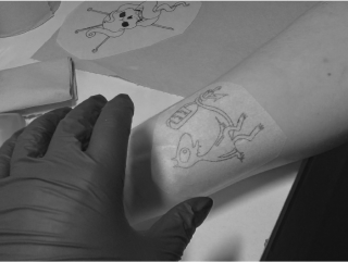 Gloved hand applying a cartoon character stencil to a client's forearm