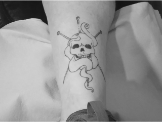 Line-work tattoo of a skull with crossed knitting needles, a crochet hook, and yarn